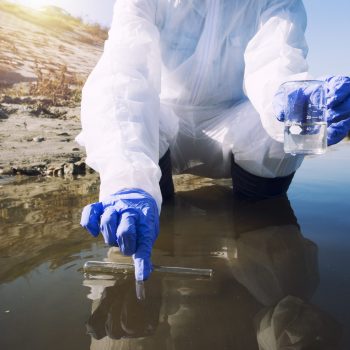 Unrecognizable ecologist taking samples of water with test tube from city river to determine level of contamination and pollution.